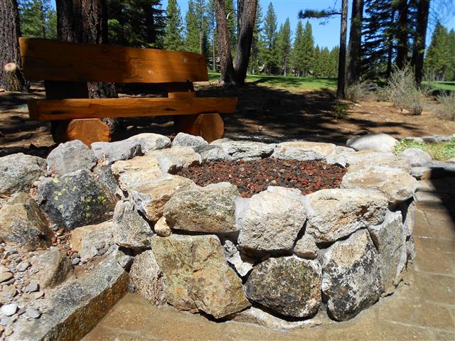 Granite boulder fire pit with lava rock and a timber bench in a pine clearing