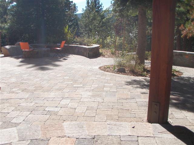 Finished stone paver patio with seating and a fire feature under pines, mountains beyond