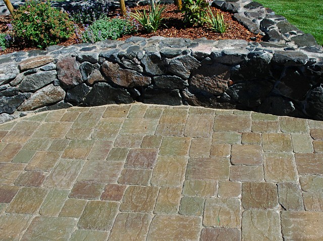 Close view of a cut stone patio meeting a dry stacked basalt retaining wall with planted bed above